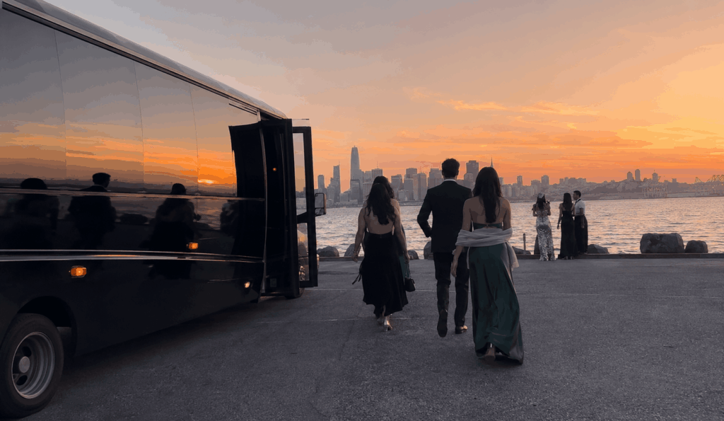 prom group taking photos near a party bus along the alameda shoreline with the bay area skyline in the background